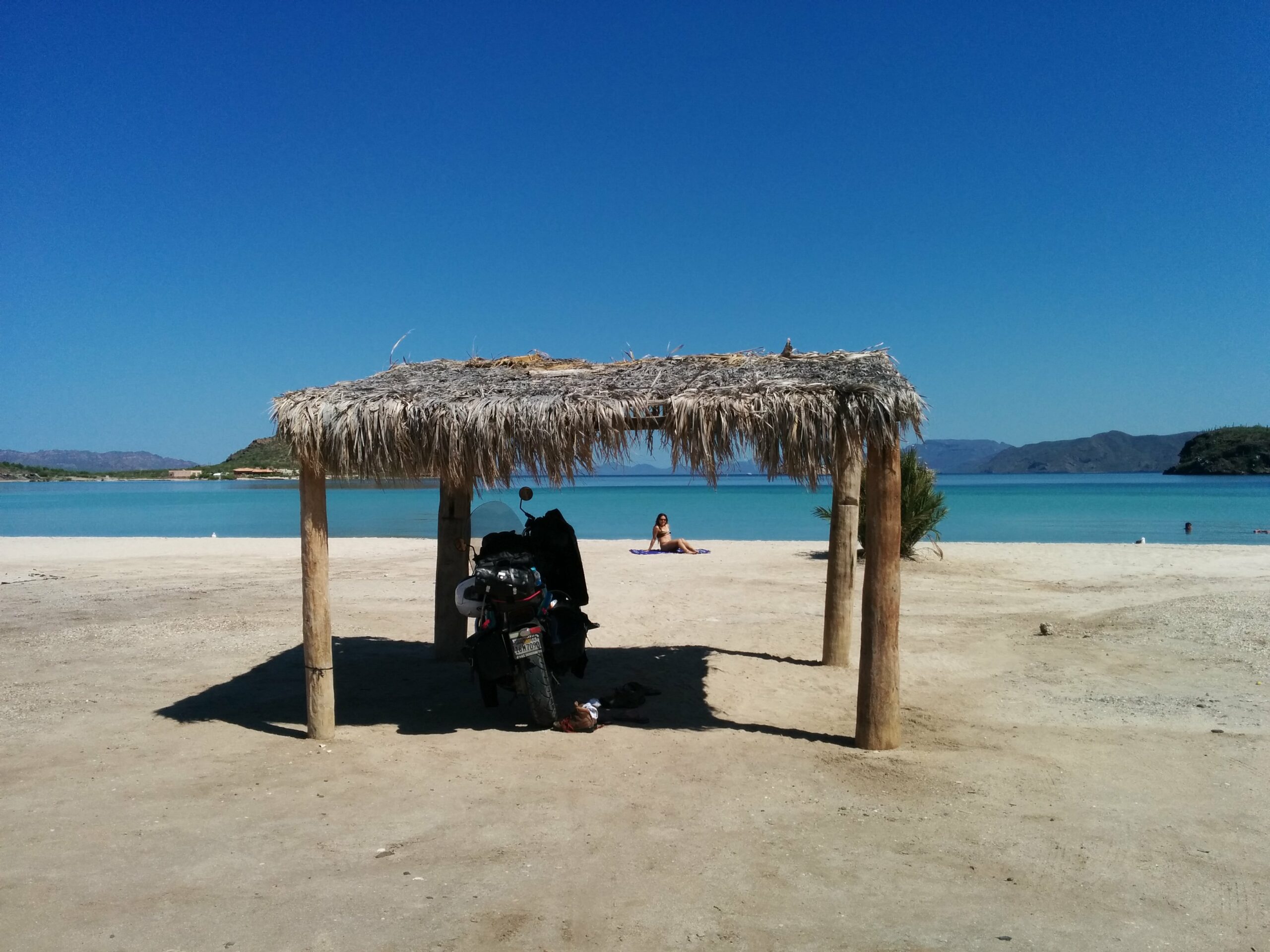 A view of Skyler's motorcycle parked beneath a cabana on a beach in Baja